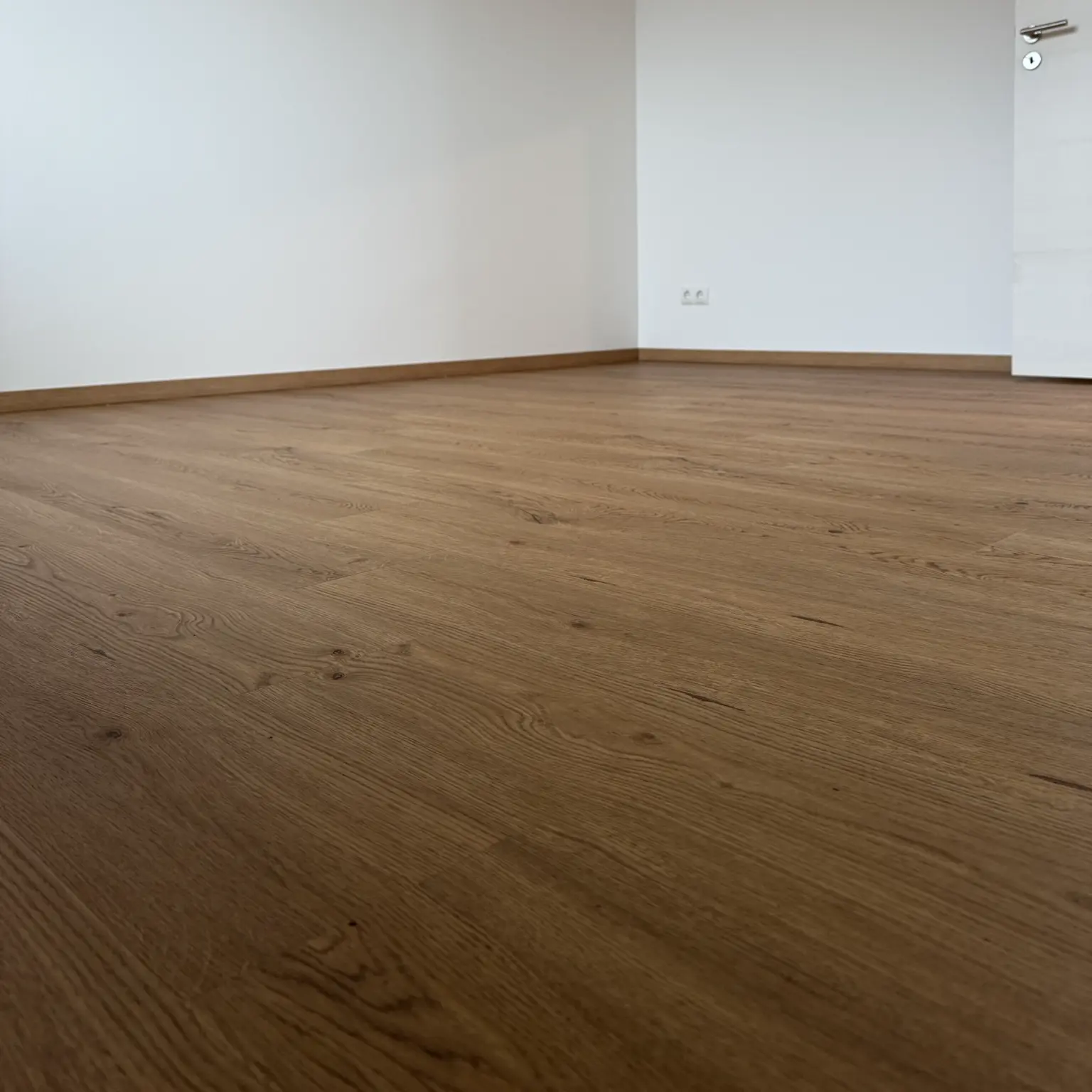 Verlegter Klebevinylboden in warmer Holzoptik mit passenden Sockelleisten und weißer Tür