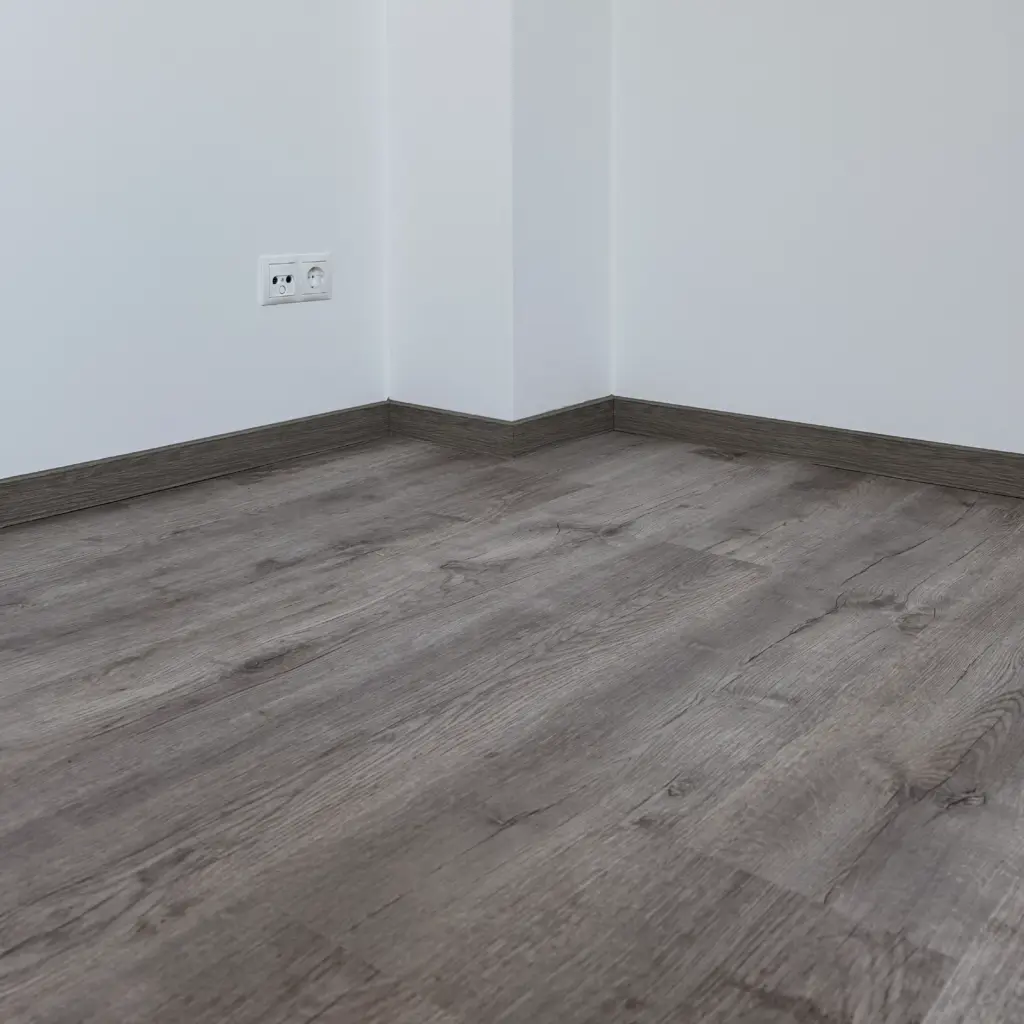 Grauer Klebevinylboden mit auf Gehrung geschnittenen Sockelleisten im Eckbereich