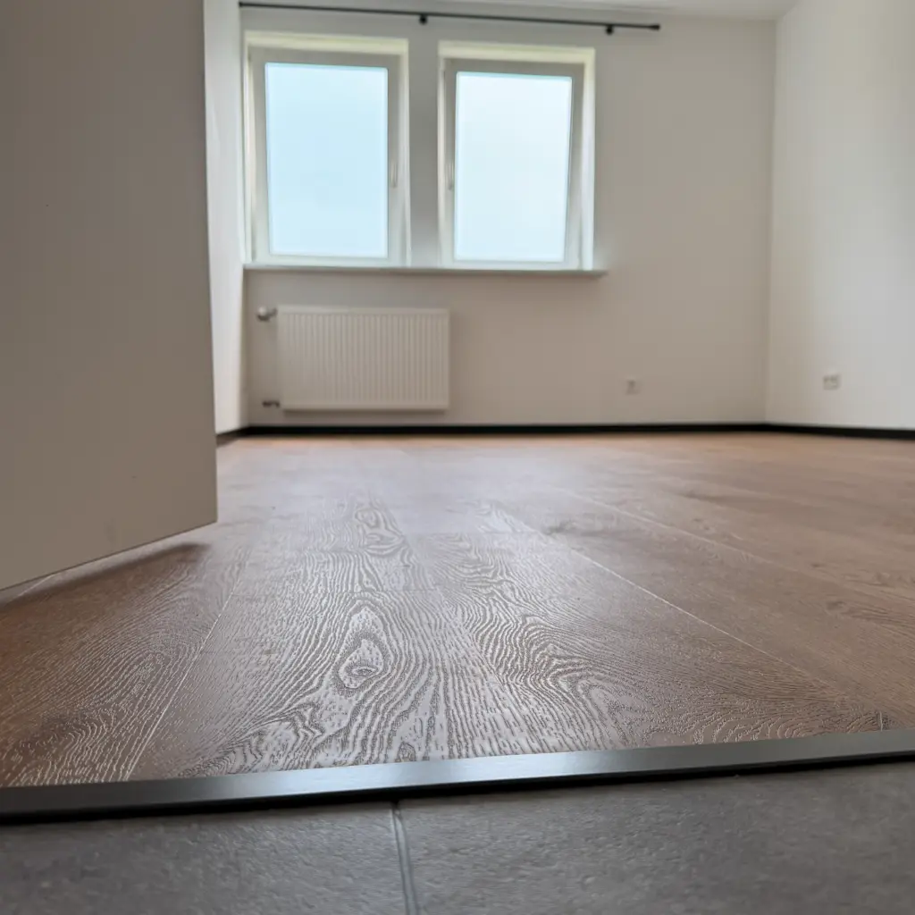 Klebevinylboden mit schwarzen Sockelleisten und Übergang zu Fliesen im Wohnraum