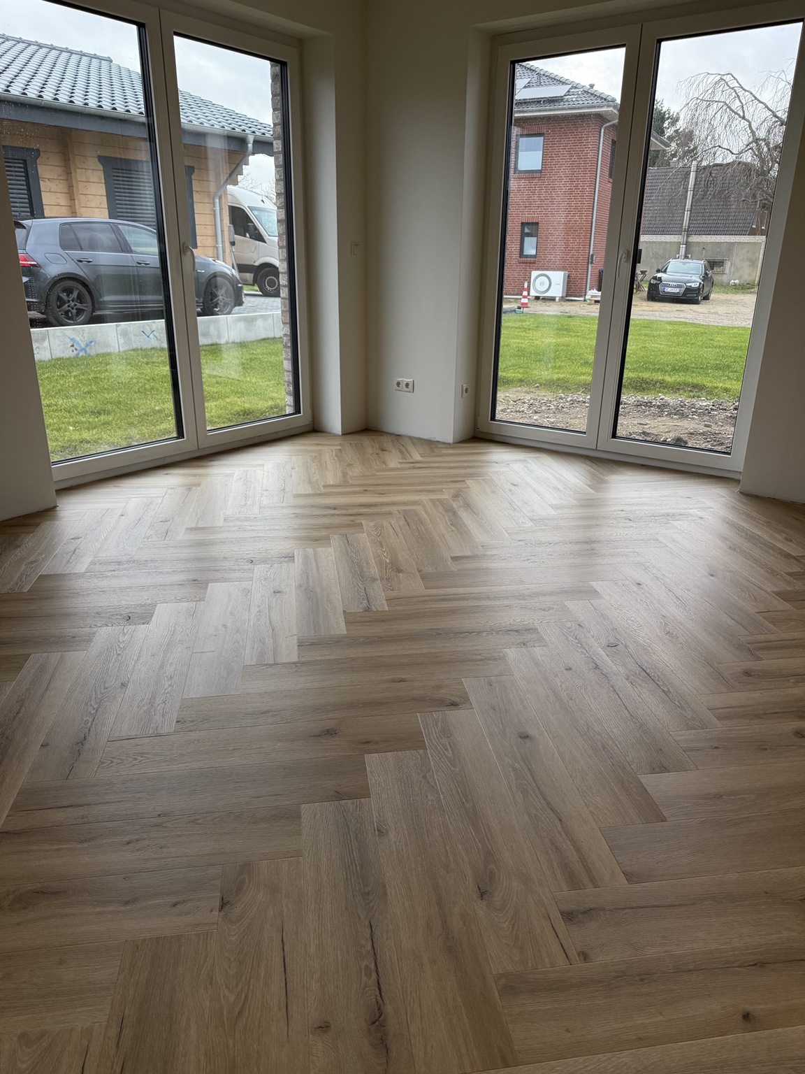 Fischgrät-Vinylboden in warmer Holzoptik vor einer bodentiefen Fensterfront