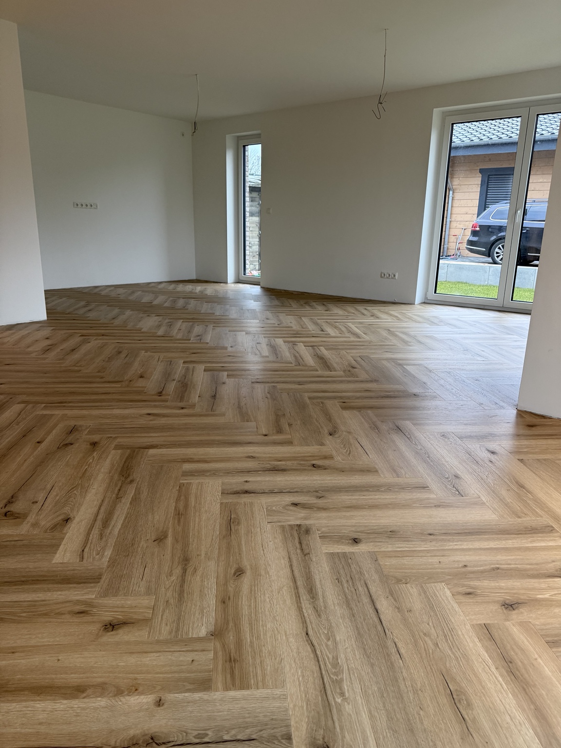 Vinylboden in Holzoptik im Fischgrätmuster in einem hellen Raum mit bodentiefen Fenstern