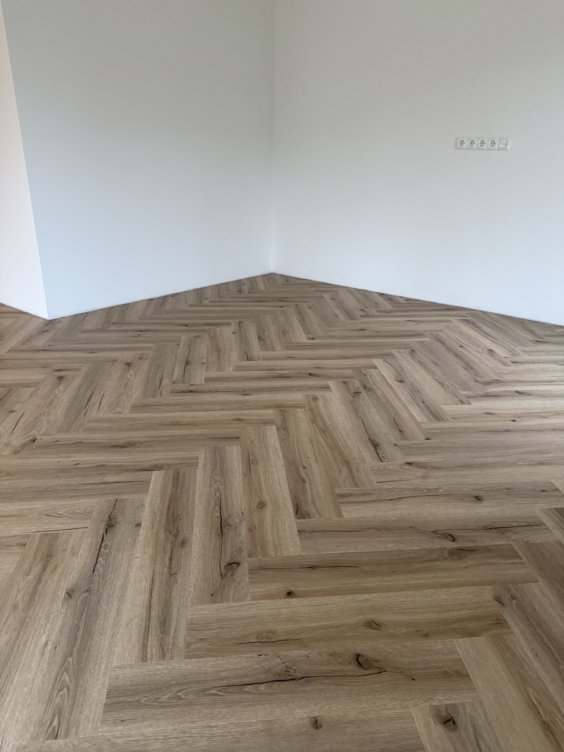 Fischgrät-Vinyl in Holzoptik mit zugeschnittenen Planken entlang weißer Wände